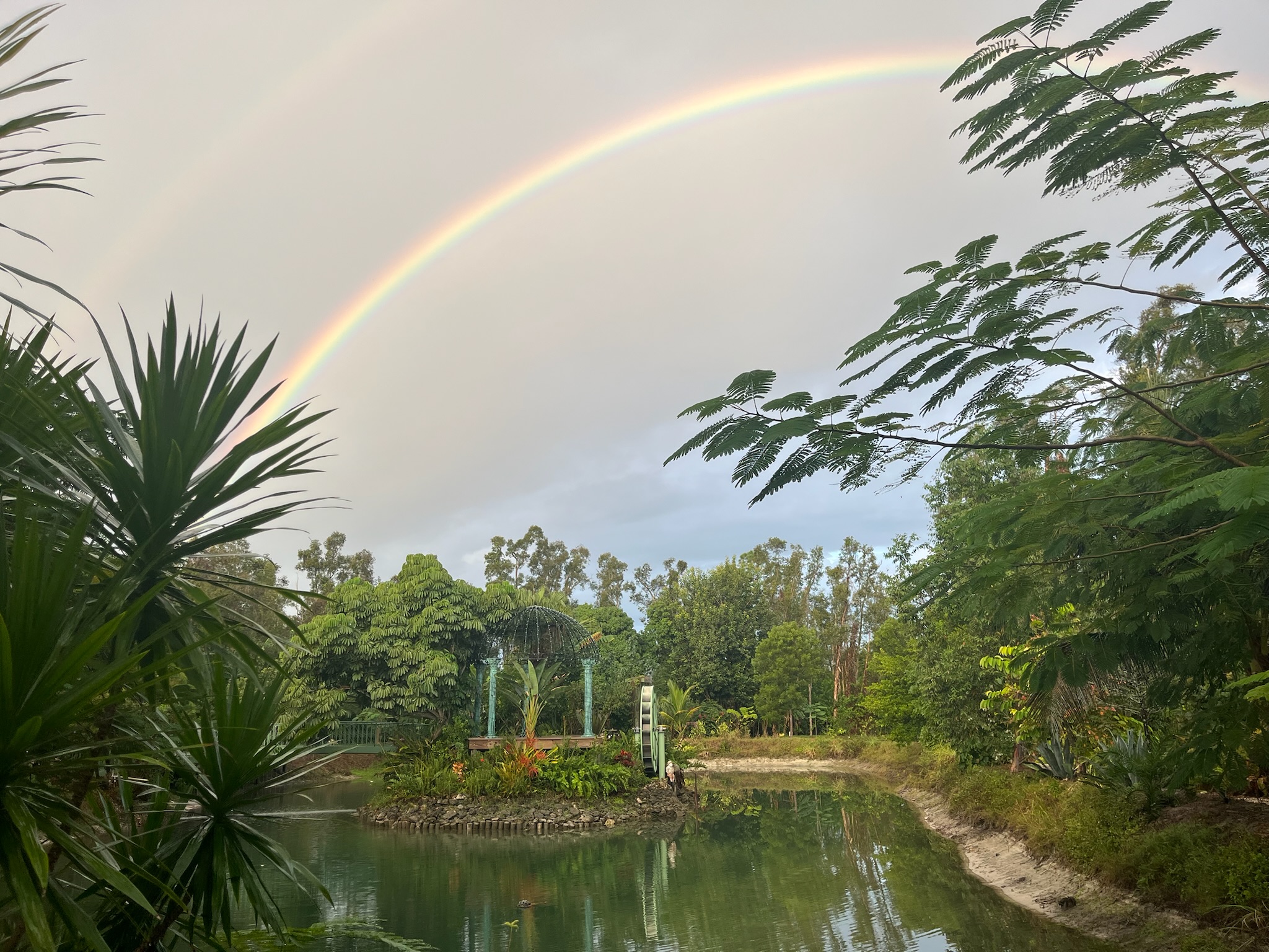 Double rainbow arching over Jane's Fruit Farm pond and tropical gardens